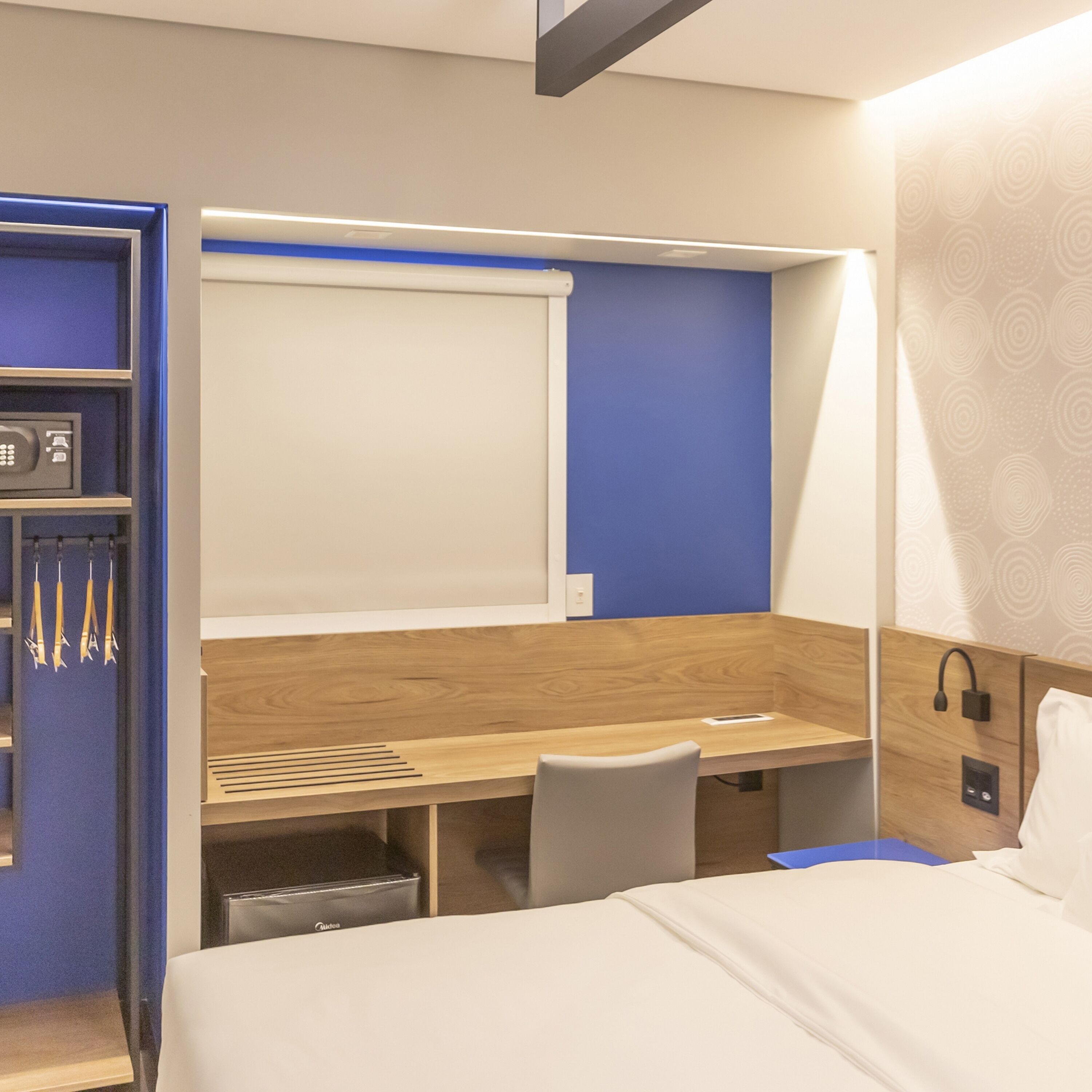 Habitación de hotel con cama, escritorio y silla. Cuenta con un mueble bajo el escritorio y un teléfono instalado en la pared.