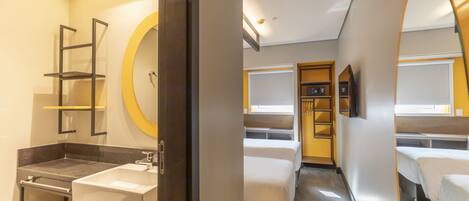 Una habitación de hotel con un baño moderno, una cama, un armario y un espejo.
