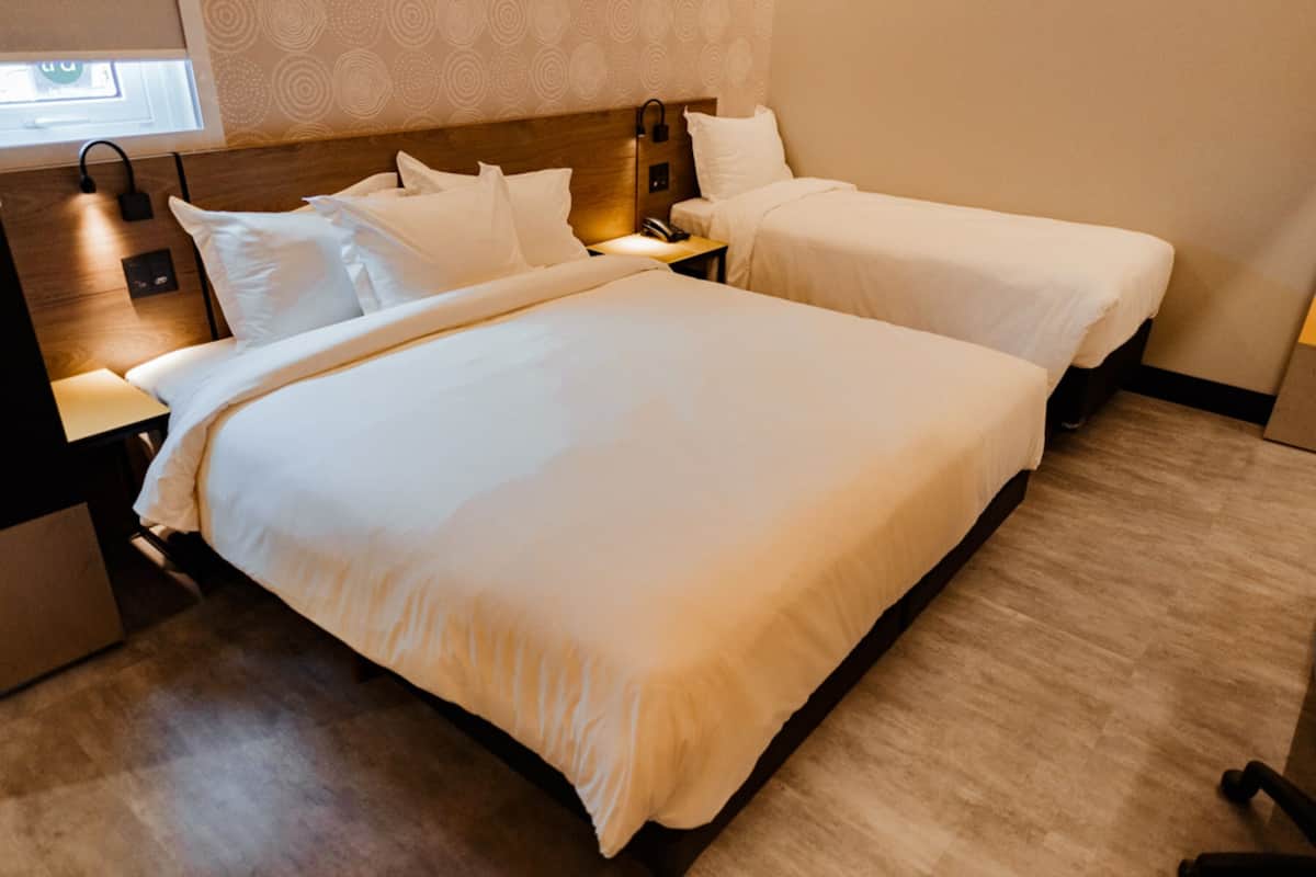 A hotel room with two single beds, a wooden headboard, bedside tables with lamps, and a wooden floor.