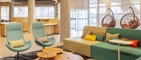 A modern lounge area with seating, a reception desk, and large windows.