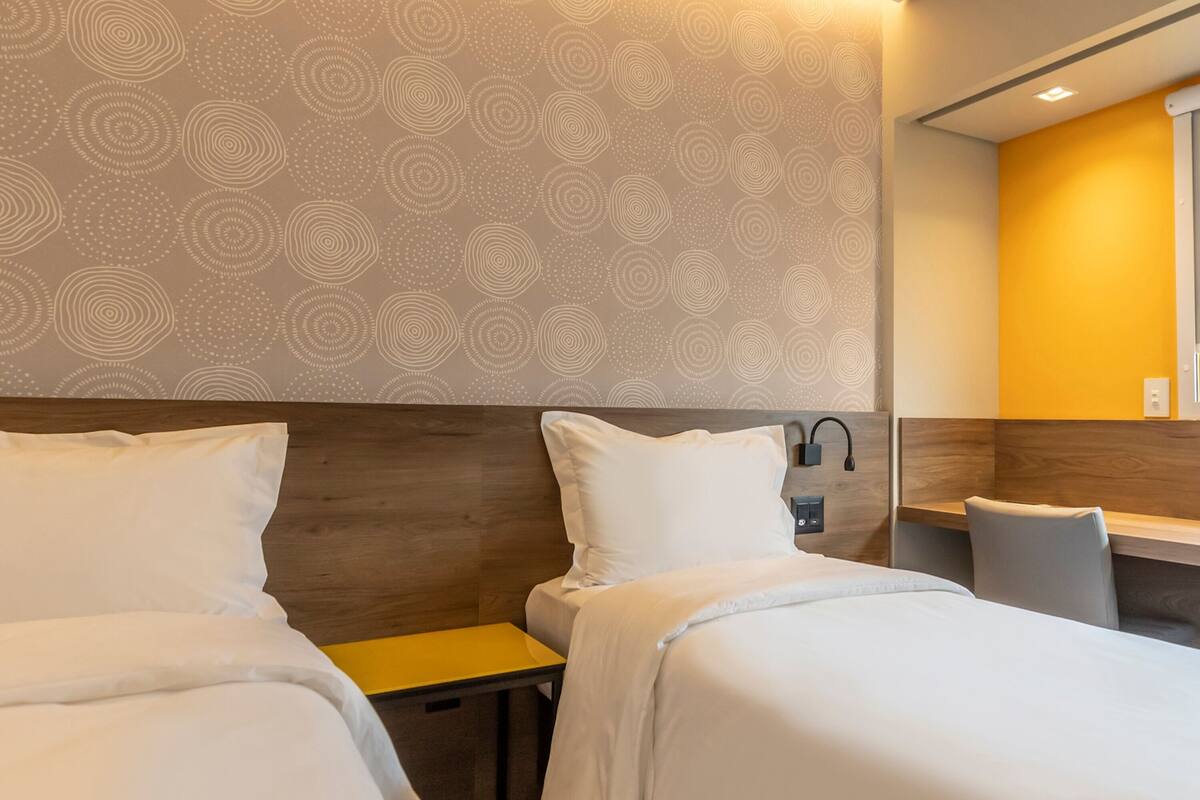 A hotel room with two beds, a wooden headboard, a small table, and a mirror.