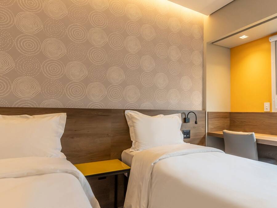 A hotel room with two beds, a wooden headboard, a small table, and a mirror.