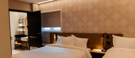 A hotel room with two beds, a desk, and a bathroom visible through an open door.