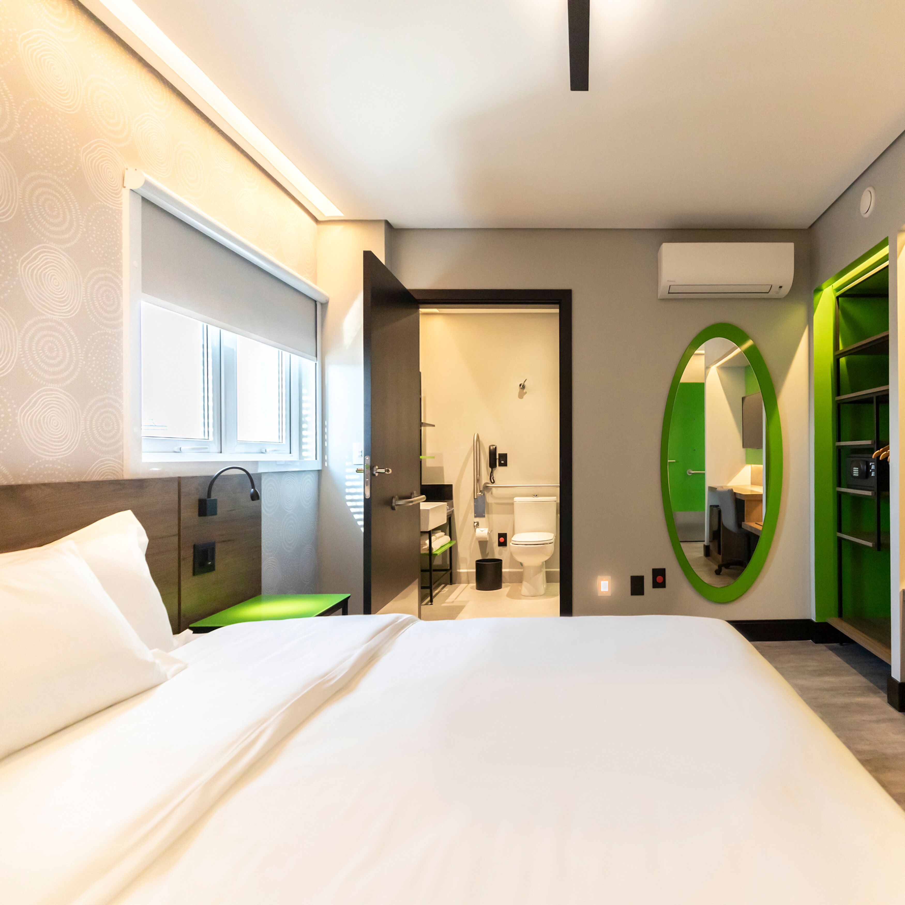 Camera d'albergo moderna con un letto grande, un bagno con il water e un lavandino, e uno specchio con cornice verde.