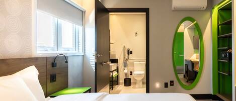 Camera d'albergo moderna con un letto grande, un bagno con il water e un lavandino, e uno specchio con cornice verde.