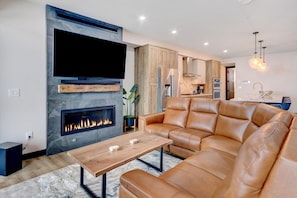 A modern living room with a fireplace, leather sofa, and a dining area. - Downtown WP River Front Villa 242 I Private Hot Tub I Views I Game Room I Discounted Attractions (Winter Park)