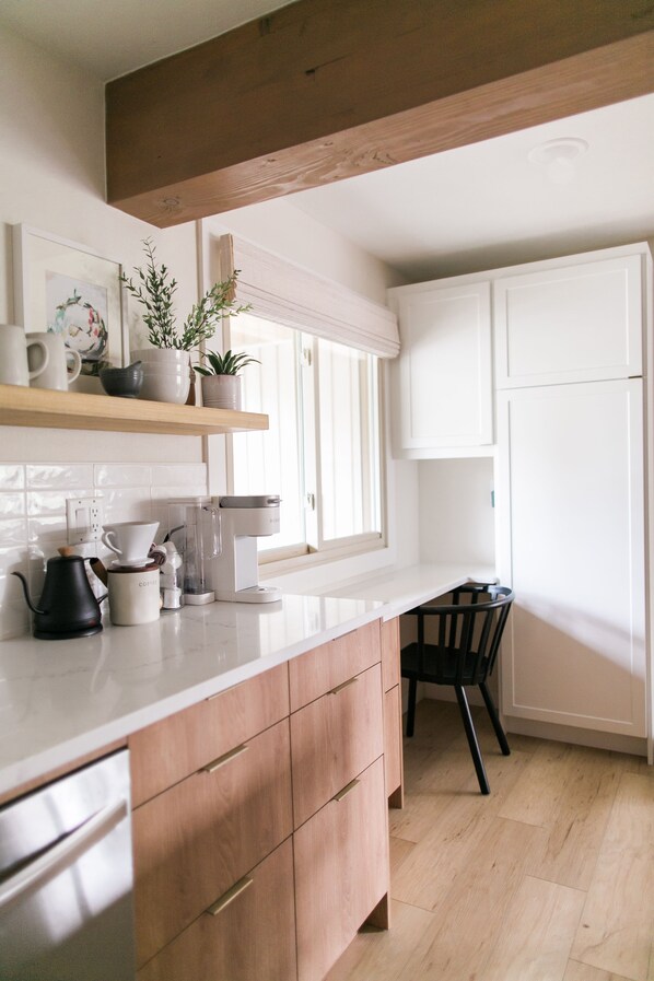A kitchen with white cabinets, a wooden countertop, a coffee maker, and a chair.