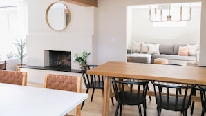 A dining area with a wooden table and chairs, a fireplace, and a sofa in the background. - Beautiful Modern Home - Heated Indoor Pool (Spokane)