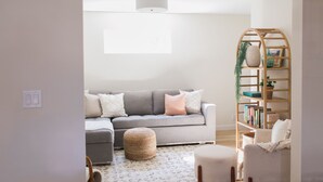 A living room with a grey sofa, ottoman, and a wooden bookshelf. - Beautiful Modern Home - Heated Indoor Pool (Spokane)