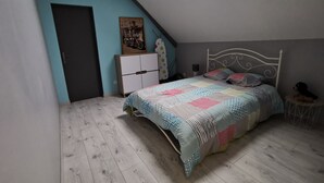 A bedroom with a sloped ceiling, a bed with patterned bedding, a dresser, a small round table, and a wall-mounted shelf. - LA GRANGE DE MELLERAY (Outarville)