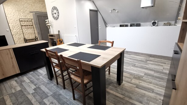 A modern kitchen with a wooden table and chairs, a stone wall, and a clock. - LA GRANGE DE MELLERAY (Outarville)