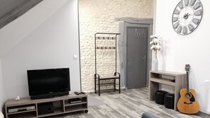 A modern living room with a flat-screen TV, a wooden coffee table, a guitar, and a stone-textured wall. - LA GRANGE DE MELLERAY (Outarville)