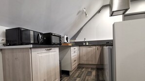 A compact kitchen with wooden cabinets, a microwave, a coffee maker, and a refrigerator. - LA GRANGE DE MELLERAY (Outarville)