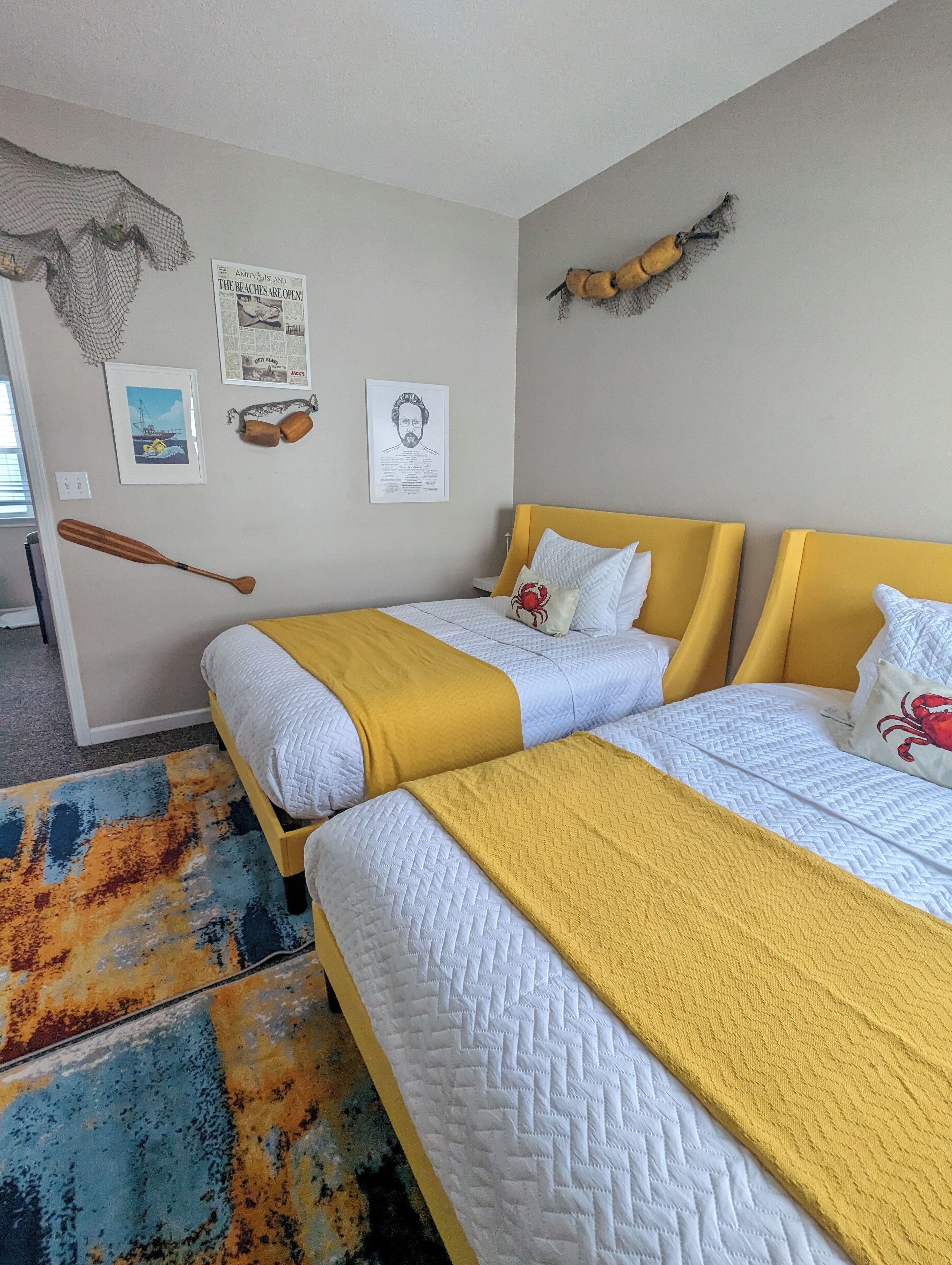 A hotel room with two beds, a wooden headboard, a yellow throw blanket, and a colorful rug.