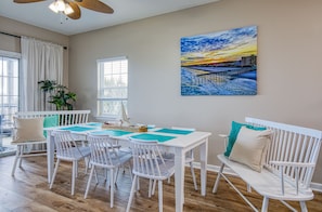 A dining area with white furniture, a painting of a sunset, and a view of the outdoors.