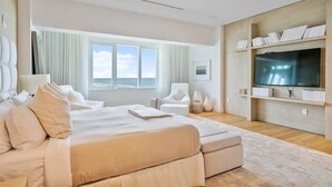 Une chambre d’hôtel moderne dotée d’un grand lit, d’un coin salon, d’une télévision et offrant une vue sur la mer.