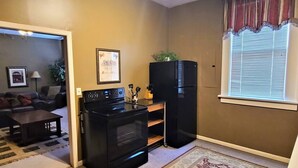 A compact kitchen with a black stove, refrigerator, and a dining area with a table and chairs. - The Westchester 1 BR located On The Bricks (Fairbury)