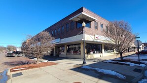 A two-story building with a storefront on the ground floor. - The Westchester 1 BR located On The Bricks (Fairbury)