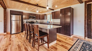 Une cuisine moderne avec un plancher en bois, des meubles de couleur sombre, des appareils électroménagers en acier inoxydable et un îlot central doté de tabourets de bar.