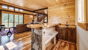 Un vaste espace de vie doté d’un îlot central en pierre, de planchers en bois et d’une grande fenêtre offrant une vue sur l’extérieur.