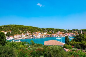 A coastal town with buildings along the waterfront, a marina with boats, and a hill with greenery in the background.