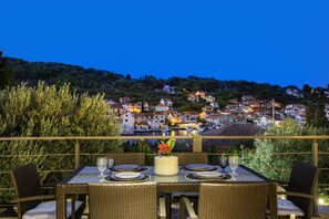 A dining table set for two with a view of a hillside town at dusk.