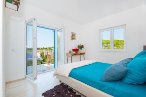 A bedroom with a bed, a small table with flowers, a window with a view, and a balcony with a chair.