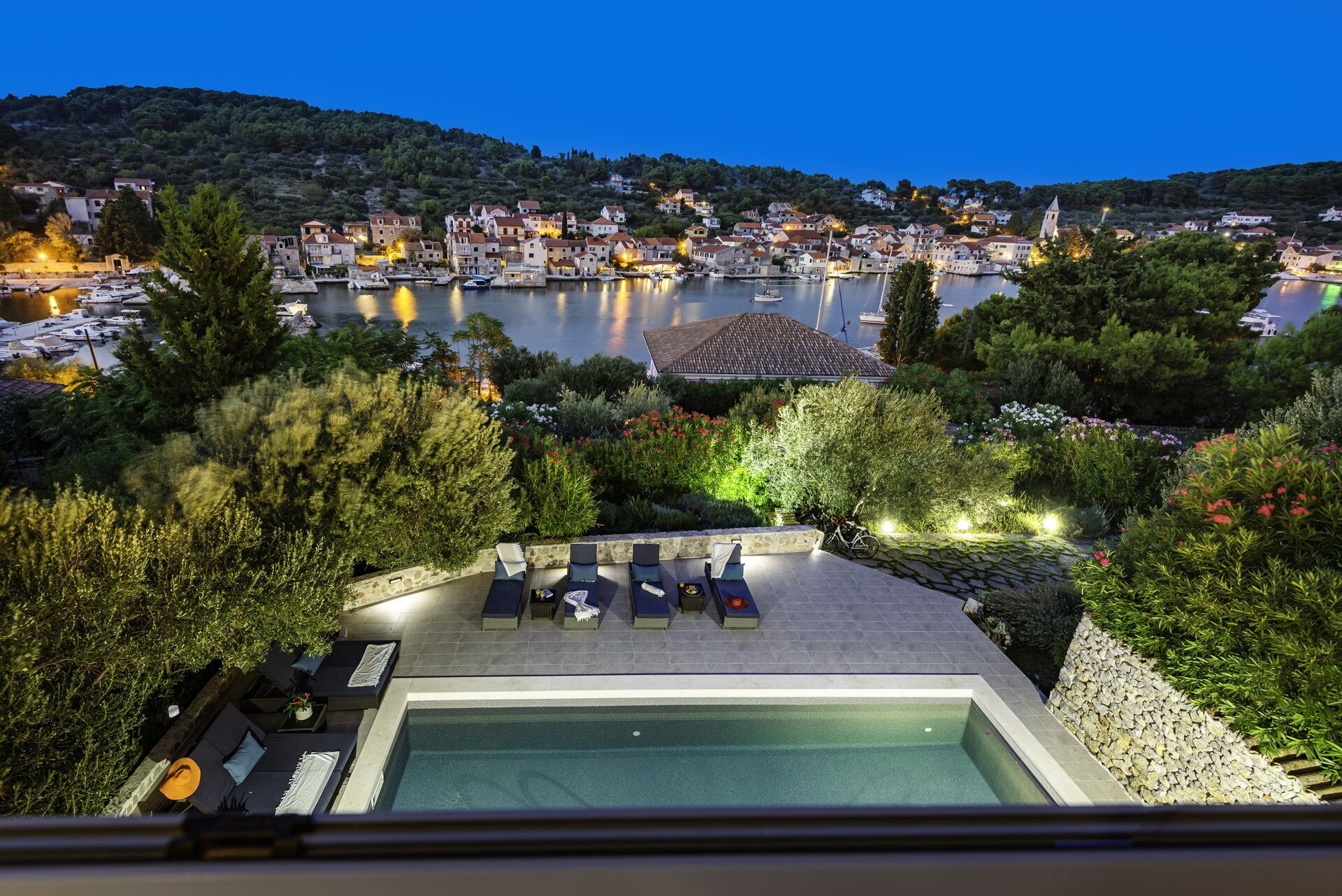 Ein Pool auf dem Dach mit Liegestühlen und Blick auf eine Stadt am See in der Abenddämmerung.