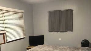 Un dormitorio con cama, televisión, ventilador y ventana con persianas.
