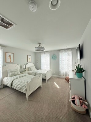 A bedroom with two beds, a ceiling fan, a mounted TV, and a potted plant. - Delaware Dreaming (Selbyville)