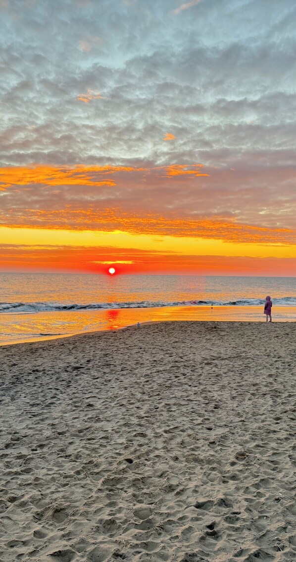 A beach with a sunset, waves, and a person standing on the sand. - Delaware Dreaming (Selbyville)