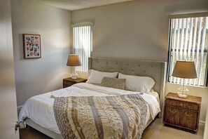 A bedroom with a large bed, two bedside tables, a window with blinds, and a framed picture on the wall. - Modern PGA West 2 bd/2ba with views, pool/spa (La Quinta)
