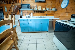 Une cuisine avec des meubles de couleur bleue, un four à micro-ondes, une cuisinière et une horloge au mur.