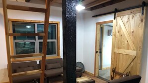 Quarto com escada de madeira, porta de celeiro deslizante, sofá e janela com persianas.