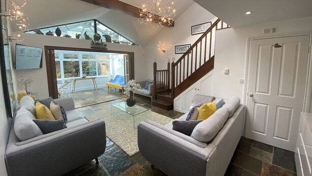 A spacious living area with a high ceiling, a glass door leading to an outdoor patio, and a staircase with wooden railings.