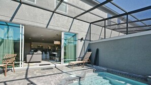 Un espace piscine extérieur moderne doté d’un patio vitré, de chaises longues et offrant une vue dégagée sur la cuisine adjacente.
