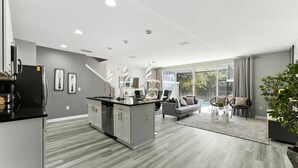 Une cuisine moderne avec des meubles gris, un îlot central et un coin repas comprenant un canapé gris et une table basse.