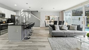 Une cuisine moderne avec un îlot central, un coin repas doté d’une table en verre et un salon avec un canapé gris.