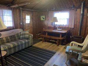 Un interior acogedor de cabaña con sofá de cuadros, una mesa de comedor, sillas de mimbre y una chimenea.