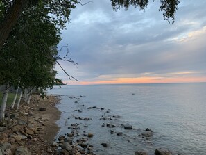 Una costa rocosa con mar en calma, una valla de madera y árboles.
