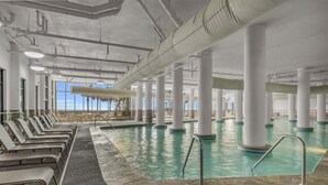 An indoor swimming pool with multiple columns, lounge chairs, and a view of palm trees. - Lazy river Beautiful northern views Sleeps 10 (Orange Beach)