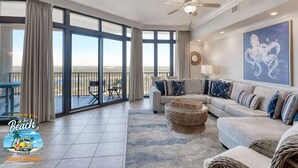 A spacious living room with a large window, a ceiling fan, a sofa set, and a view of the beach. - Lazy river Beautiful northern views Sleeps 10 (Orange Beach)