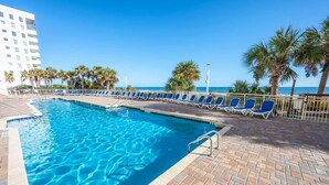 A swimming pool with blue water, surrounded by lounge chairs and palm trees, with a building in the background. - Bay Watch 503 Direct Oceanfront w/ Tiki Bar, Pools (North Myrtle Beach)