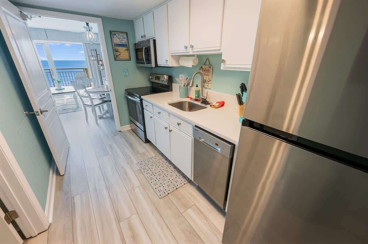 A kitchen with white cabinets, stainless steel appliances, and a view to the outside.