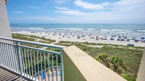 A balcony with a view of a beach with people and umbrellas. - Bay Watch 503 Direct Oceanfront w/ Tiki Bar, Pools (North Myrtle Beach)