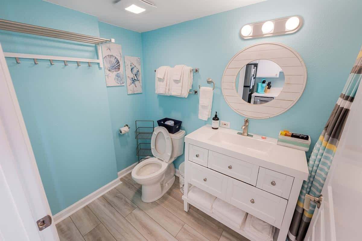 A bathroom with a toilet, sink, and mirror. There are towels hanging on a rack and a shower curtain.