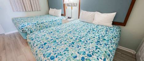 A hotel room with two beds, each with a floral bedspread, a nightstand with a lamp, and a painting on the wall.