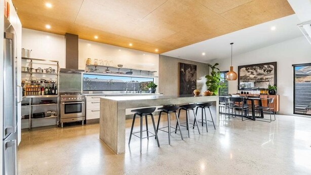 A modern kitchen with a central island, bar stools, and a dining area with a view. - Enjoy the deluxe swimming pool surrounded by a poolside sundeck (Lennox Head)