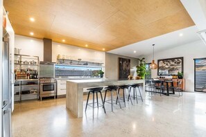 A modern kitchen with a central island, bar stools, and a dining area with a view. - Enjoy the deluxe swimming pool surrounded by a poolside sundeck (Lennox Head)