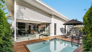 A modern house with a swimming pool, outdoor seating, and a covered patio area. - Enjoy the deluxe swimming pool surrounded by a poolside sundeck (Lennox Head)